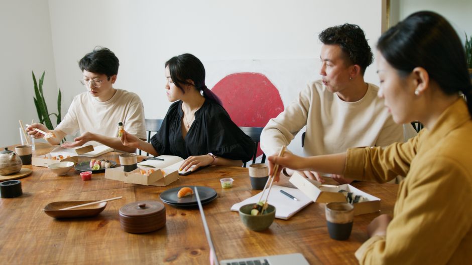 A group of coworkers enjoying sushi during a casual indoor meeting.